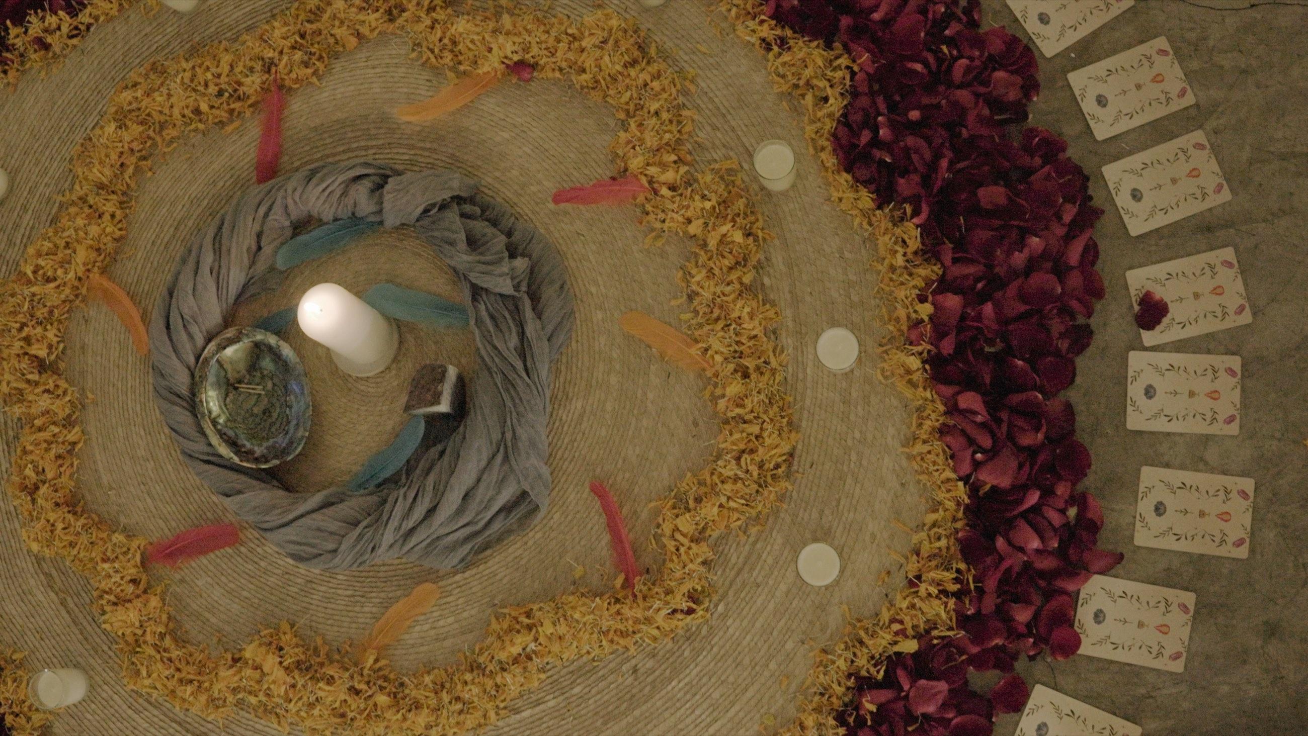 Mandala de ceremonia visto desde arriba: cempasúchil, pétalos de rosa, veladoras y cartas ilustradas alrededor de una vela encendida